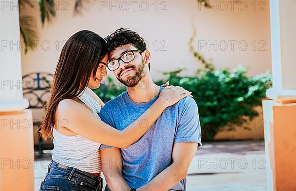 Attractive girl tenderly hugging her boyfriend outdoors. Girl hugging her boyfriend while he smiles at her