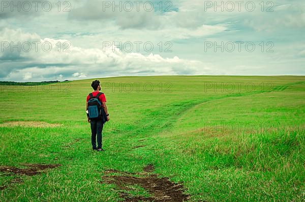 View of traveler man on a beautiful road in the countryside. Young explorer man walking in a green field