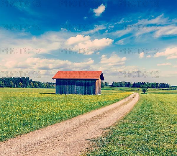 Vintage retro effect filtered hipster style image of rural road in summer meadow with wooden shed. Bavaria