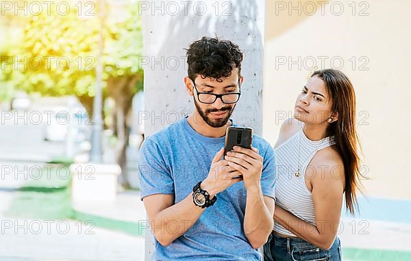 Suspicious girl spying on her boyfriend phone. Jealous girl spying on her boyfriend's cell phone in the park
