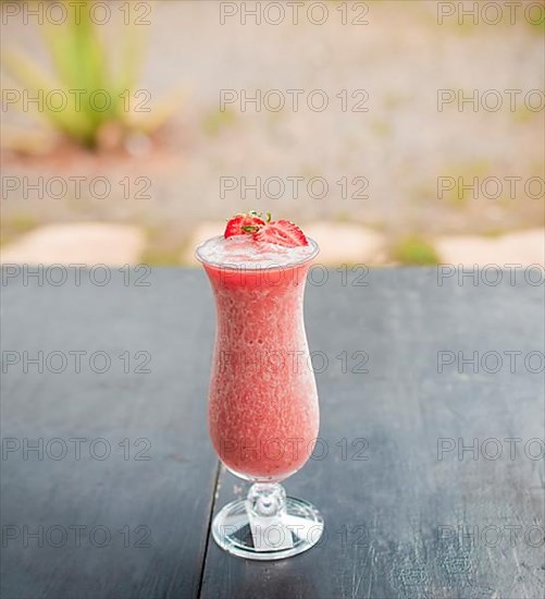 Strawberry milkshake on wooden table with blurred background. Close up of healthy strawberry smoothie on wood with blurred background