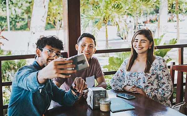 Young friends taking a selfie in a coffee shop. Three happy people in a coffee shop taking a selfie. Front view of teenage friends taking selfie and having fun in a cafe restaurant