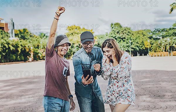 Three cheerful people looking at cell phone outdoors