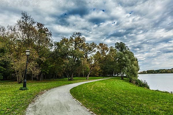 Path in autumn park near the lake with dramatic sky