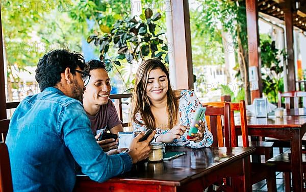 Young friends in a coffee shop with their cell phones having a good time. Three people in a coffee shop with phones having a good time. Three teenage friends on their cell phones in a coffee shop