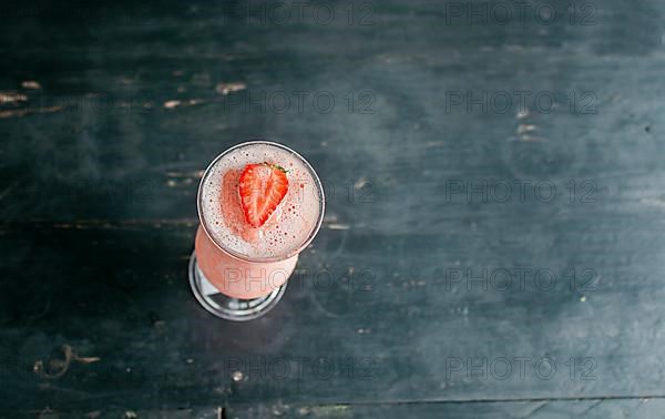 Top view of strawberry smoothie on dark wooden table. View of strawberry milkshake on dark wood. View from above of delicious strawberry smoothie with a strawberry on top on wood