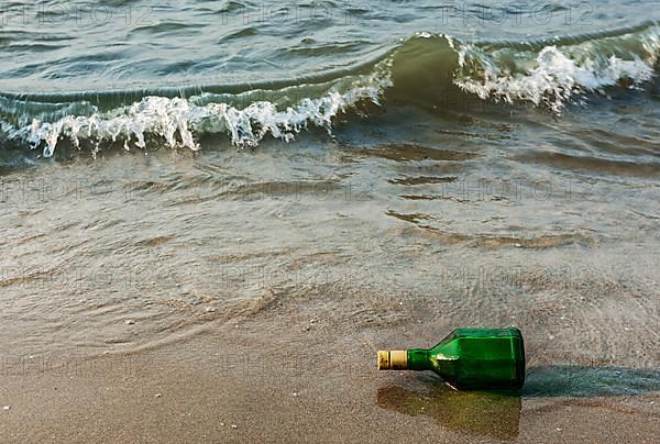 Message bottle on beach sand in waves