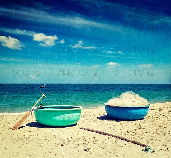 Vintage retro hipster style travel image of fishing coracle boats on beach with grunge texture overlaid. Mui Ne