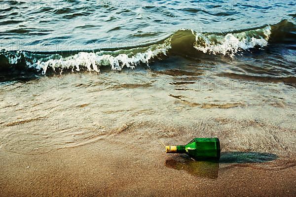 Vintage retro hipster style travel image of message bottle on beach sand in waves