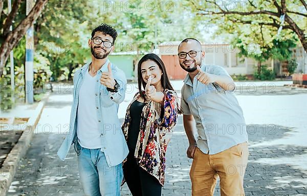 Three happy friends giving thumbs up on the street. Three smiling teenagers giving thumbs up on the street. Team concept of smiling friends giving thumbs up on the street