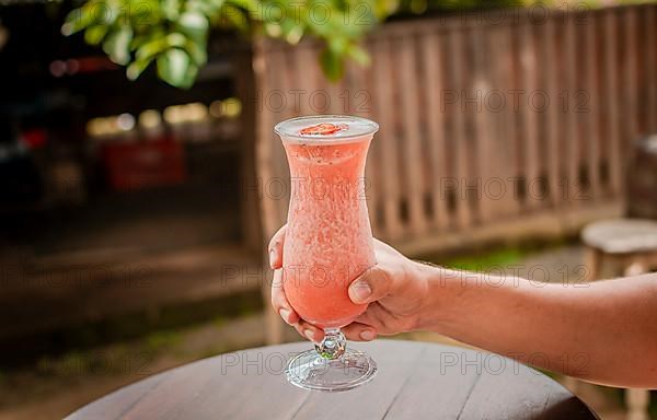 Hands showing strawberry smoothie on wooden table. People hand holding a strawberry milkshake on wood