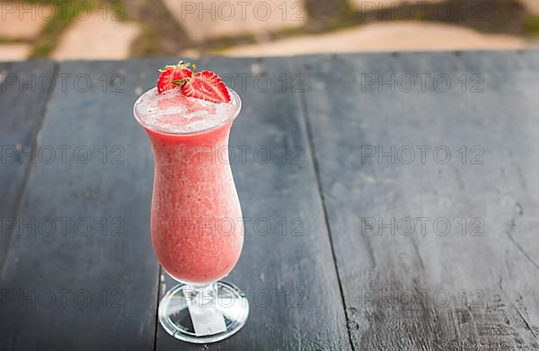 Strawberry smoothie on wooden table. Strawberry milkshake on wooden table with blurred background. Close up of healthy strawberry smoothie on wood with blurred background