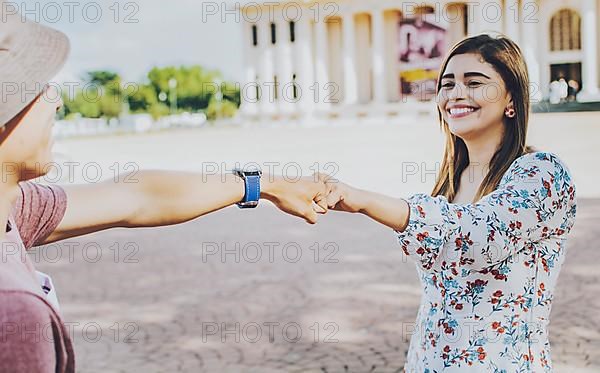 Two young smiling teenagers bumping fists in the street. Close up of guy and girl shaking fists in the street. A guy and girl shaking hands on the street