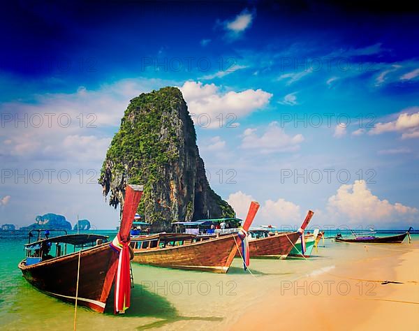 Vintage retro effect filtered hipster style travel image of long tail boat on tropical beach with limestone rock