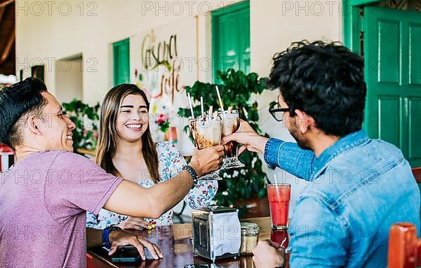 Happy friends enjoying a milkshake in a coffee shop. Three happy best friends meeting and toasting in a coffee shop