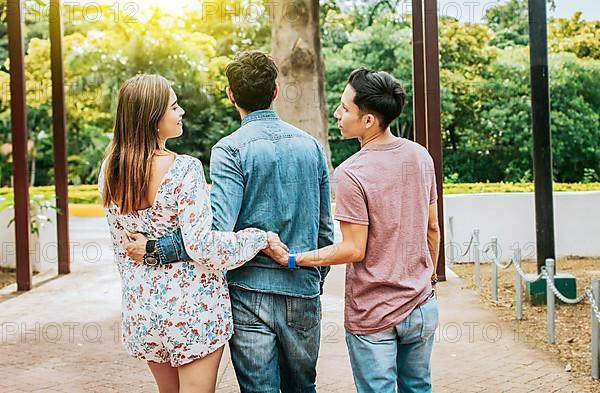 Unfaithful girl walking in the park with her boyfriend while holding another man hand. Love triangle concept. Woman holding hands with another man while walking with her boyfriend outdoor