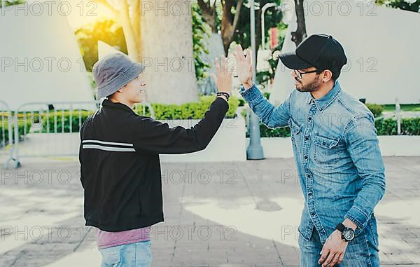 Side view of people greeting each other and shaking hands on the street. Two teenage friends shaking hands outdoors. Concept of two friends greeting each other with a handshake on the street