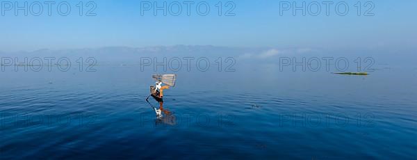 Panorama of traditional Burmese fisherman balancing with fishing net at Inle lake