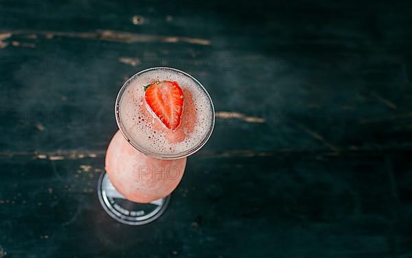 View of strawberry milkshake on dark wood. View from above of delicious strawberry smoothie with a strawberry on top on wood. Top view of strawberry smoothie on dark wooden table