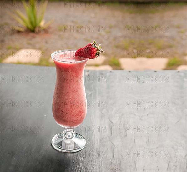 Healthy strawberry smoothie in glass on dark wood. Strawberry milkshake on dark wood with blurred background. Close-up Delicious strawberry smoothie with strawberry pieces on wood