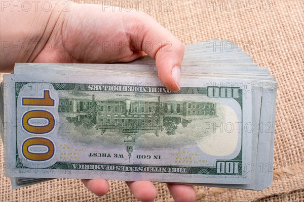 Hand holding banknote bundle of US dollar on a linen canvas background