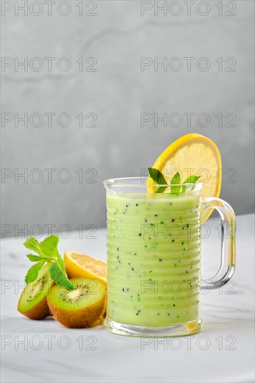 Cup with kiwi and lemon smoothie with mint on marble background