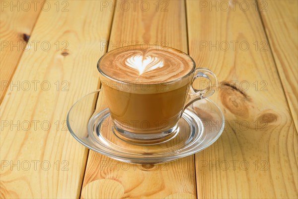 Cappuccino in transparent glass cup on wooden table