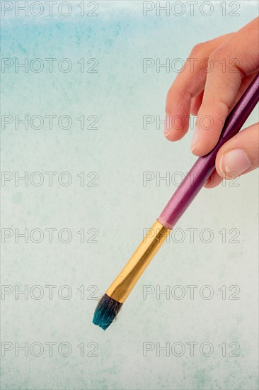 Hand holding a paint brush on water covered with foam