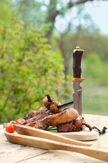 Grilled ribs and champignon on skewer served with fresh cucumber and tomato on wooden table outdoor