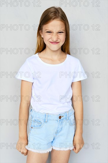 Young angry and mischievous girl in white t-shirt and jeans shorts posing in studio