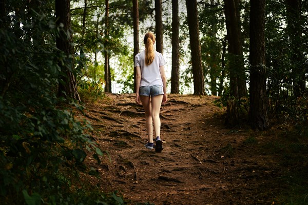 Back view of a young woman hiking along a forest path