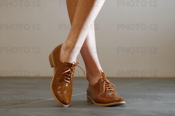 Cropped image of bare female legs in patent leather shoes with shoelaces