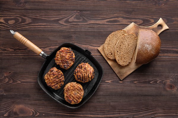 Top view of cast iron grill pan with beef cutlets and freshly baked brown bread