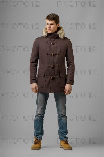 Full length portrait of handsome man in warm coat with hood posing in studio