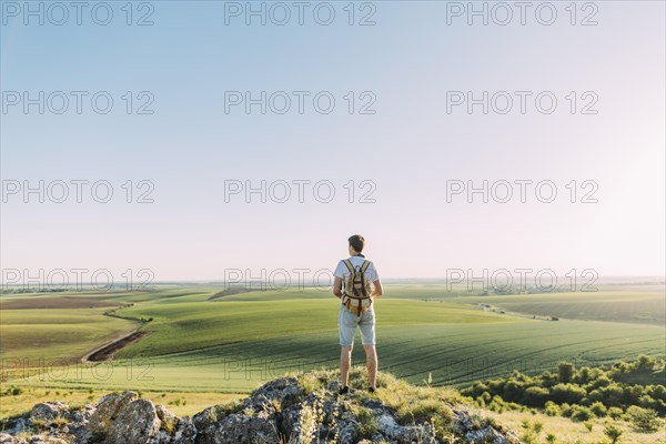 Rear view male hiker with backpack looking green rolling landscape