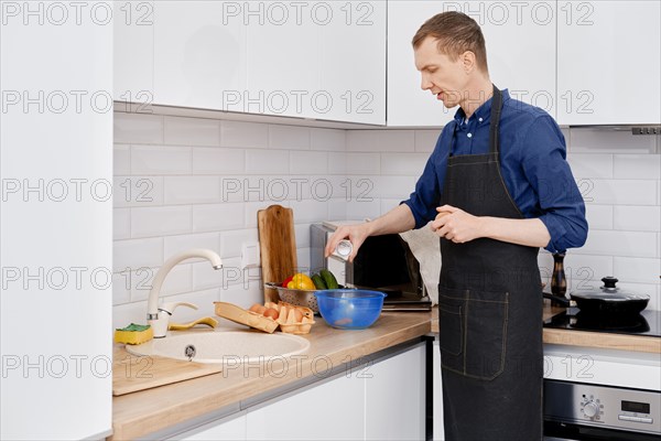 Middle-aged man pours salt making an omelet in the kitchen