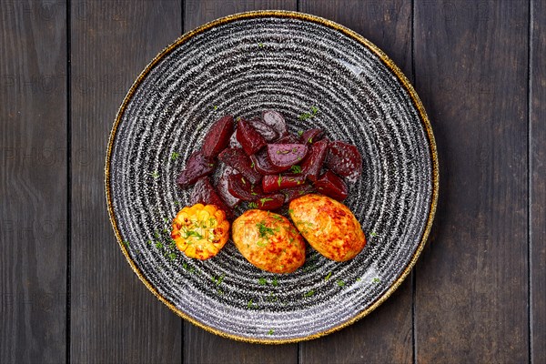 Top view of plate with fried pork cutlet with roasted beetroot slices and grilled maize on dark wooden table