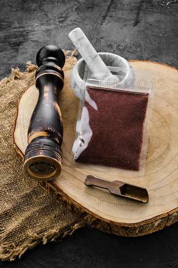 Wooden cross section with sumac in plastic package and stone mortar and mill