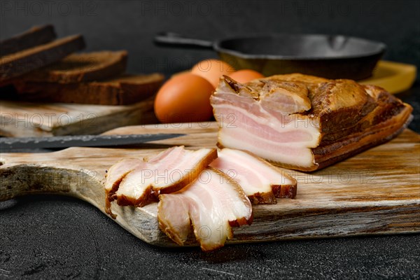 Closeup view of smoked pork bacon with brown bread and eggs on wooden cutting board