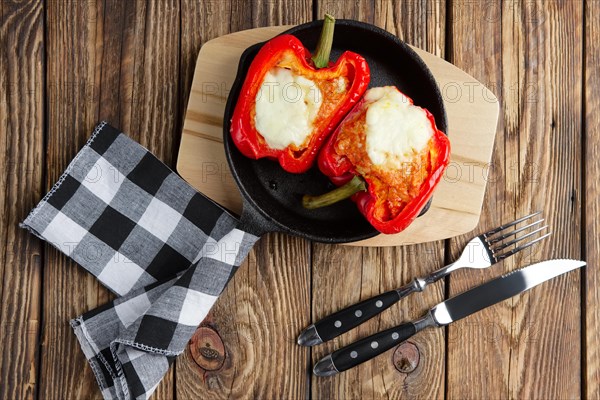 Bell pepper stuffed with meat with melted cheese mozzarella on top baked in oven in cast iron skillet. Top view. Natural wooden background