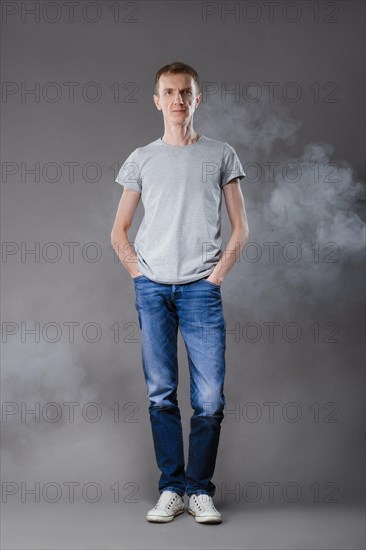 Middle age man in jeans with hands in pockets and t-shirt on gray background