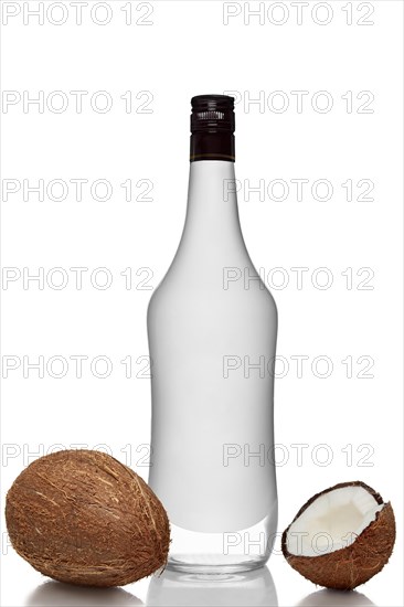 Bottle of alcohol beverage with coconut flavour with whole and opened coconuts with reflection on white background