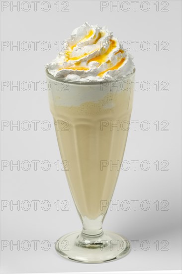 Mango and lemon milkshake summer cocktail in tall facetted glass on gray background