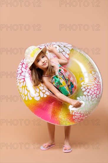 Cute child in sundress and straw hat with swimming ring playing in studio