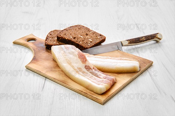 Top view of two slices of bacon and brown bread on wooden cutting board