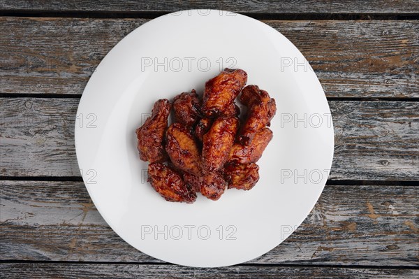 Tasty grilled chicken wings Buffalo on a white dish on wooden table
