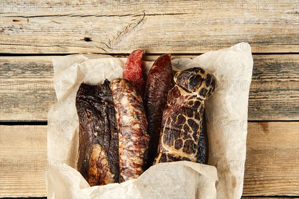 Smoked and dried meat and sausages sticking out of wrapping paper on wooden table