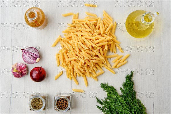 Overhead view of penne pasta with spice and herbs on wooden background