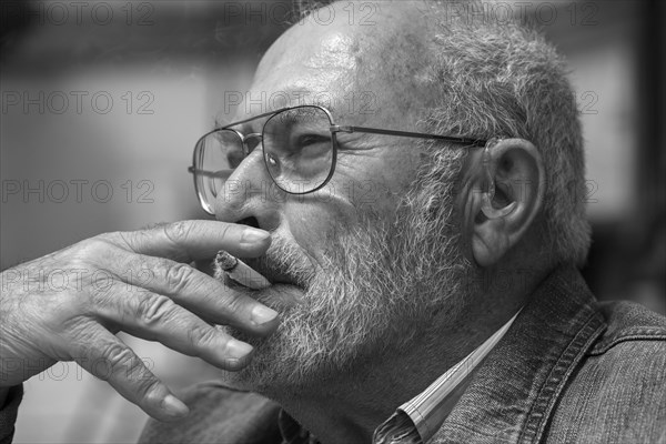 Portrait of a smoking gentleman with beard and hearing aid in ear