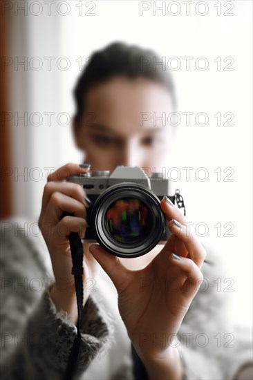 Blurred girl with photo camera in her hands on sofa near window